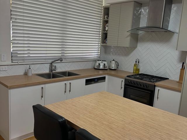 White kitchen with a timber-tone island benchtop and black bar stools